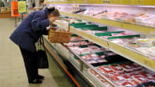 Nainen tutkii lihatuotteita marketin tiskillä.