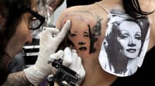 Tatuoija tekee Marlene Dietrichin kuvaa nuoren naisen selkään.