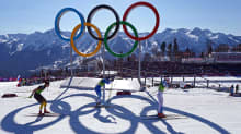 Naiset hiihtävät olympiarenkaiden ohi.
