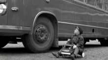 Pieni poikaa ajaa leikkiautolla linja-auton vieressä.
