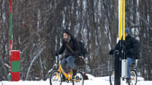 Kaksi pakolaista käyttää polkupyörää ylittäessään rajan Venäjältä Norjaan.