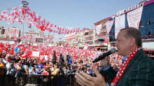 Recep Tayyip Erdoğan on kuvan oikeassa laidassa etualalla. Hän puhuu oikeassa kädessään olevaan mikrofoniin ja elehtii vasemmalla kädellään. Hänellä on tumma ruutukuvioitu pikkutakki ja puolueensa - sekä Turkin lipun - väreissä oleva kaulaliina. Yleisömeressä heiluu suuri määrä Erdoğanin puolueen lippuja.