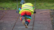 Lapsi keinuu värikkäissä vaatteissa päiväkodin keinussa.