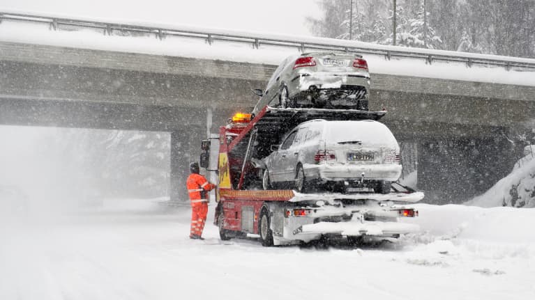 Kolaroituja autoja nostetaan hinausauton kyytiin lumisateessa moottoritiellä.