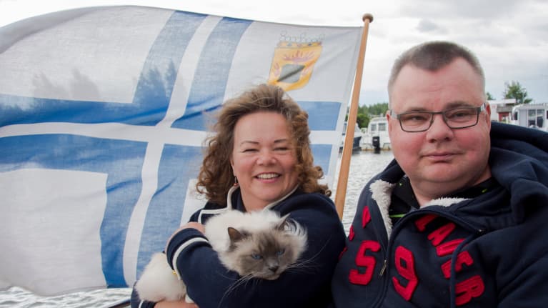 Päivi Kant-Bergroth ja Mikael Bergroth istuvat kissansa Jussin kanssa tuulisen veneen kannella.