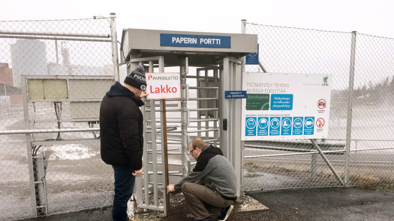 Kaksi miestä poistavat Paperiliiton lakkokylttiä UPM:n Kymin paperitehtaan portilta Kouvolassa.