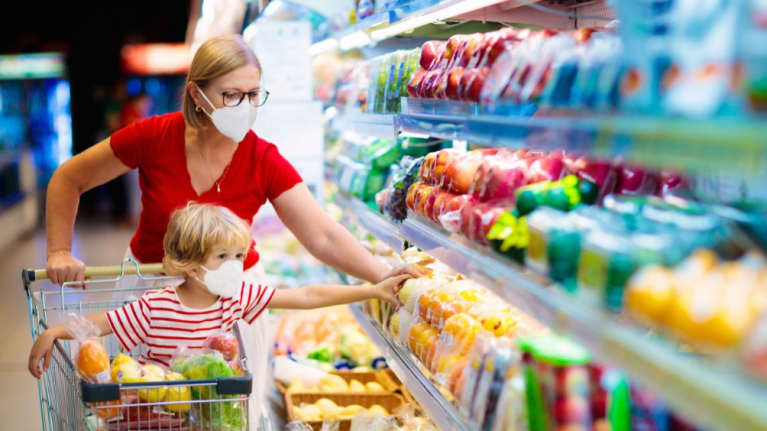 Nainen ja lapsi ruokakaupassa. Lapsi istuu ostoskärryissä. Molemmilla on hengityssuojain. 