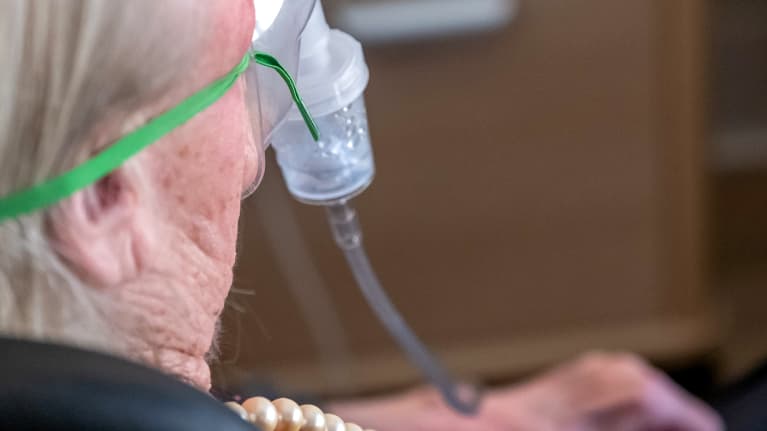 Lähikuva vanhuksesta takaapäin. Vanhuksella happimaski.