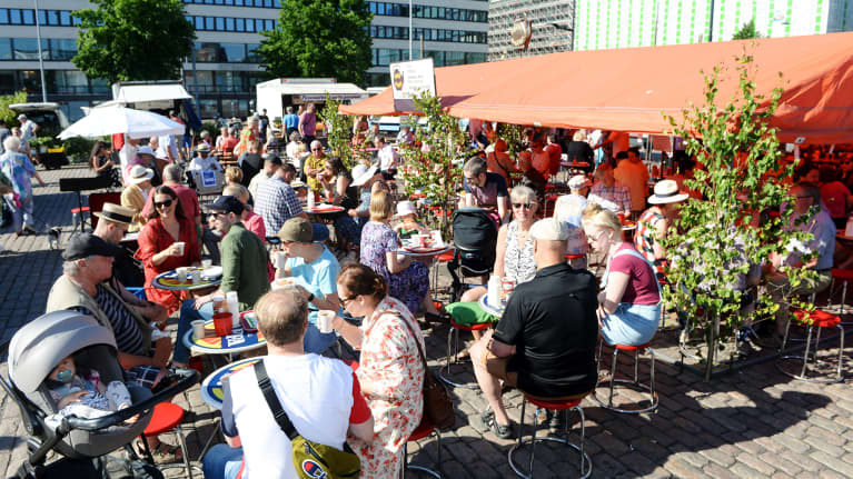 Ihmisiä juhannusaattoaamun torikahveilla Hakaniemen torilla Helsingissä.