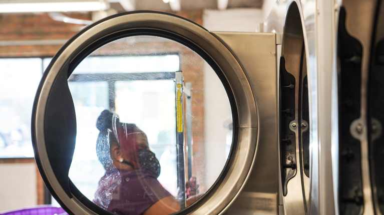 Asiakas pesukoneen aukinaisen oven läpi kuvattuna.