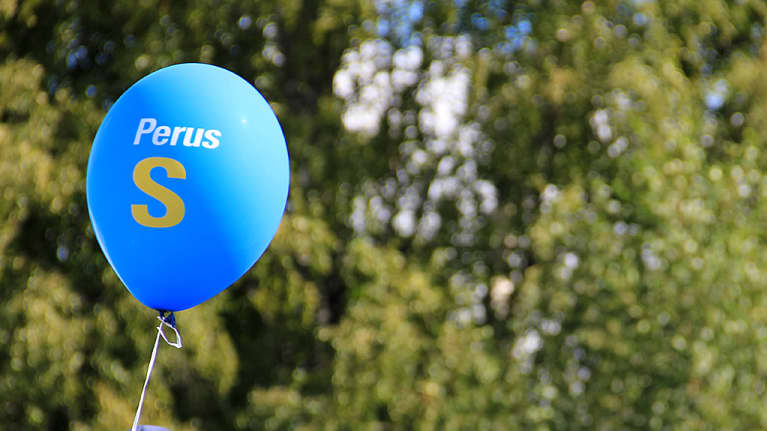 Kuvassa sininen Perus S ilmapallo vihreää vehreää taustaa vasten. 