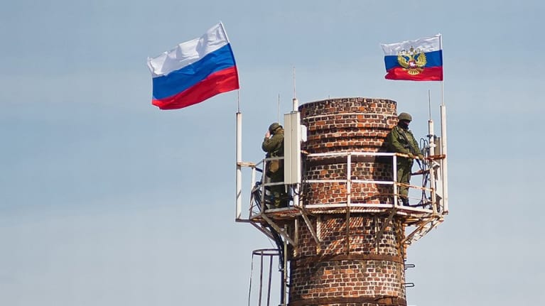 Kaksi venäläissotilasta ja Venäjän lippua suuren savupiipun päässä.