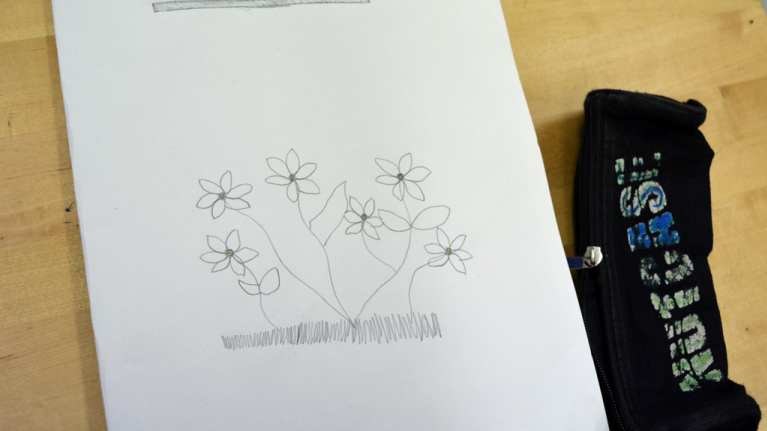 Oppilaan kuvittama kasvion kansi ja penaali pulpetin päällä.