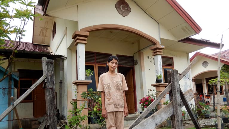 nainen seisoo talonsa edessä