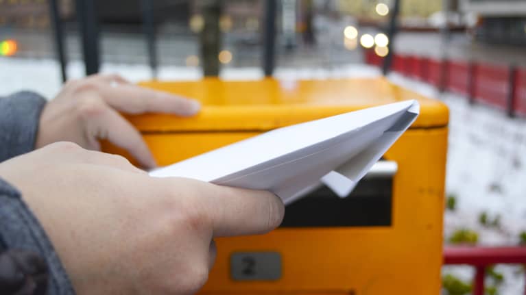 Ihminen työntää kirjekuorta postin laatikkoon.