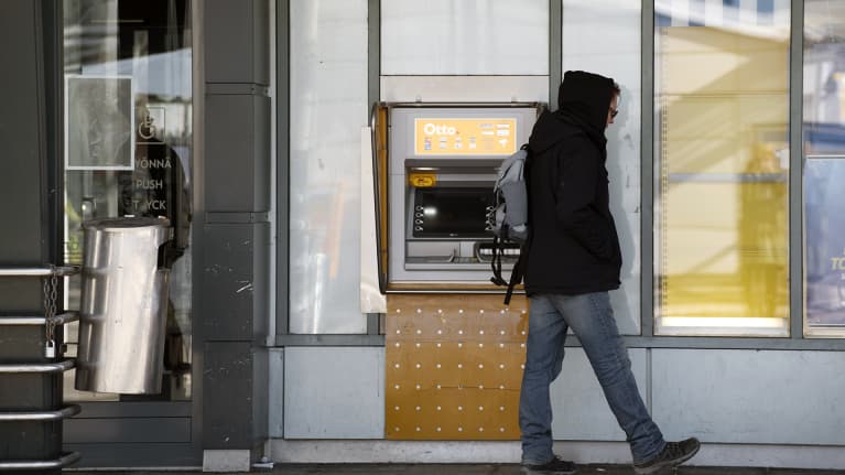 Mies seisoo raha-automaatin edustalla.