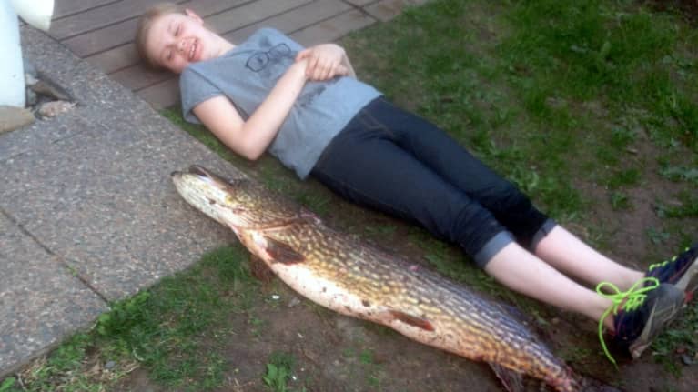 Tyttö makaa nurmikolla vieressä pitkä ja iso hauki