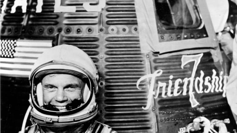 Mustavalkoinen kuva, John Glenn hymyilee avaruskypärä päässään.