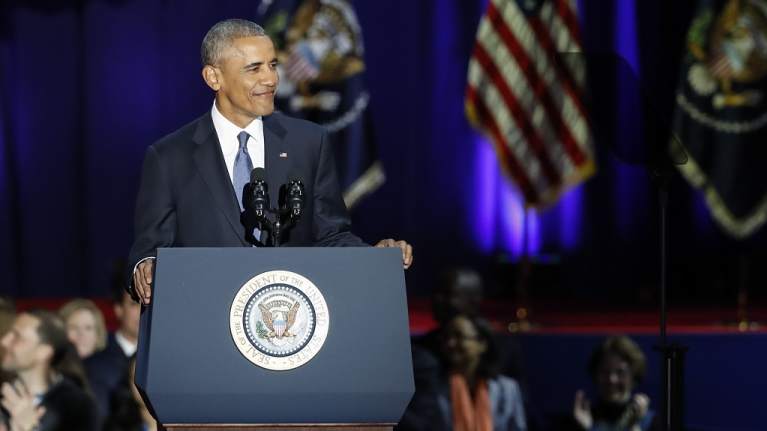Obama hymyilee puhujapöntössä.
