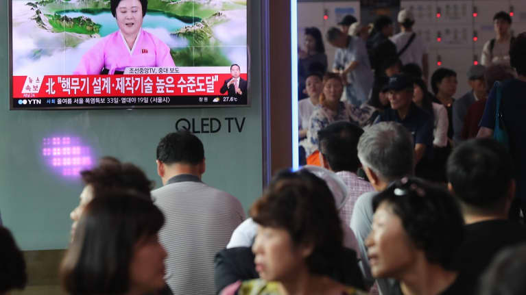 Eteläkorealaiset katsovat televisiota, jossa näkyy pohjoiskorealainen uutisankkuri vaaleanpunaisessa asussa.