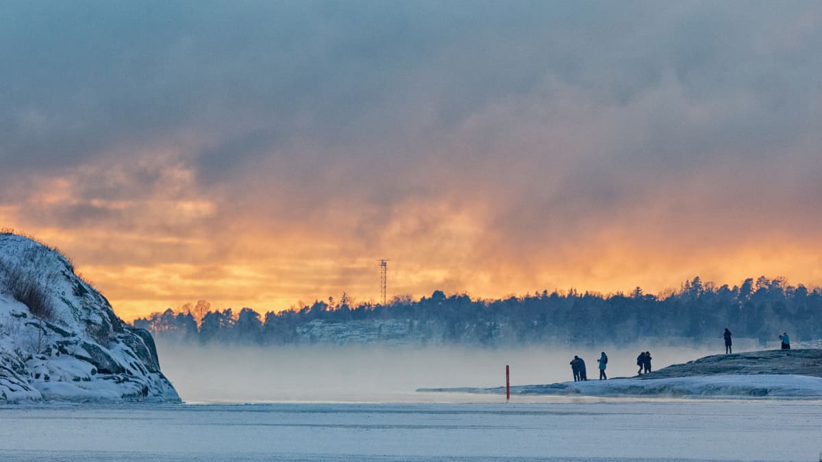 Ihmiset ihailemassa auringonlaskua ja merisumua Helsingissä.