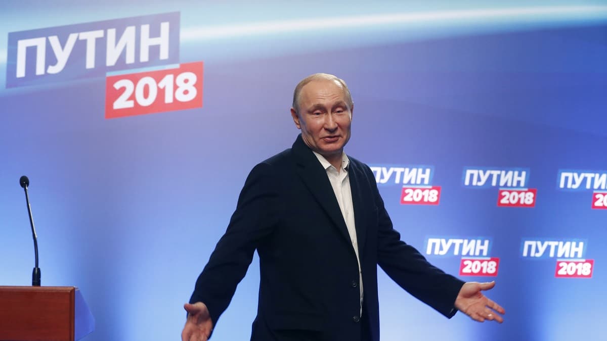 Vladimir Putin puku yllään, levittelee käsiään.