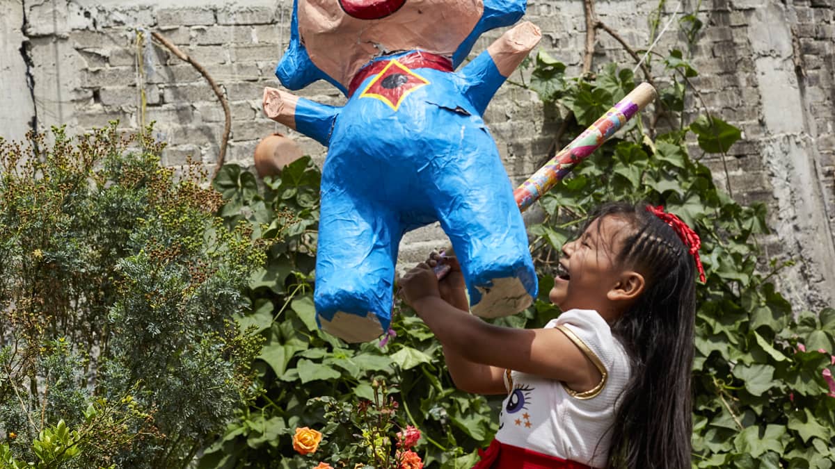 Tyttö lyö karkilla täytettyä piñata-nukkea lastenjuhlissa Chalcossa.
