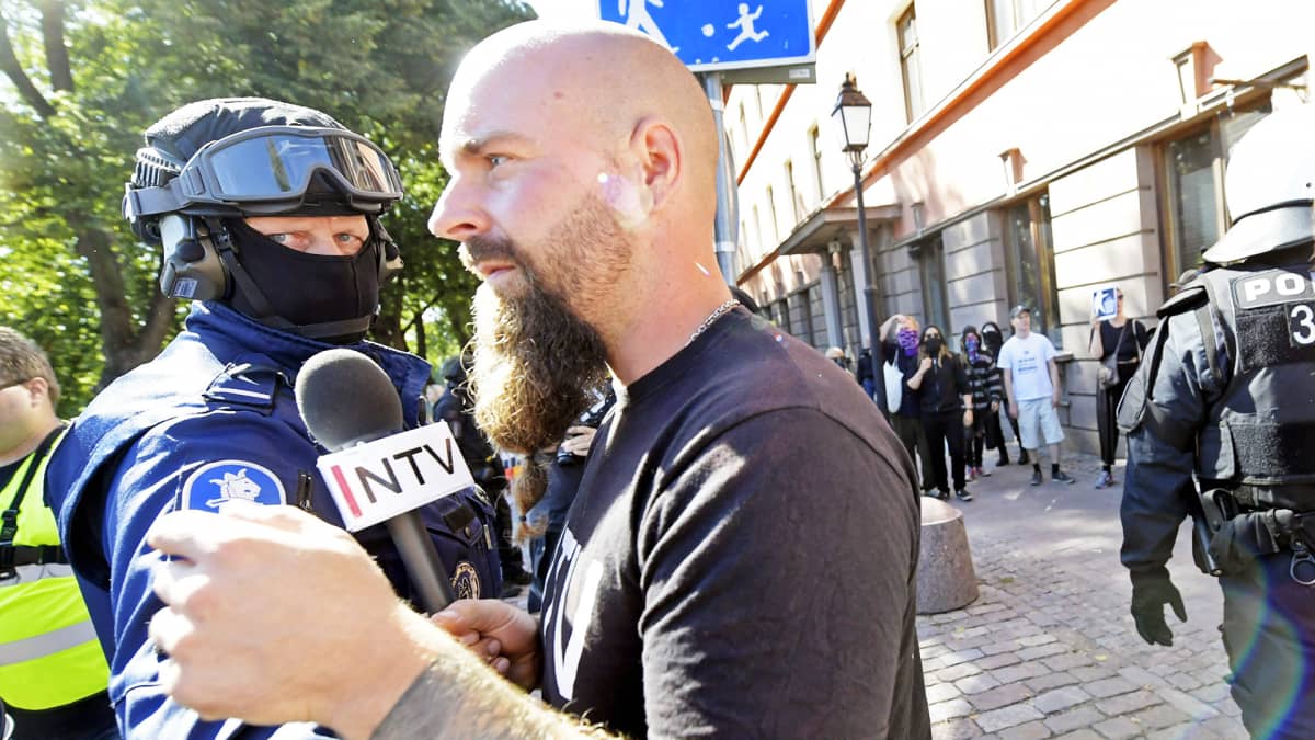 Poliisi estää uusnatsien Pohjoismaisen vastarintaliikkeen NTV-kanavan toimittajana esiintynyttä miestä menemästä vastamielenosoittajien luokse.