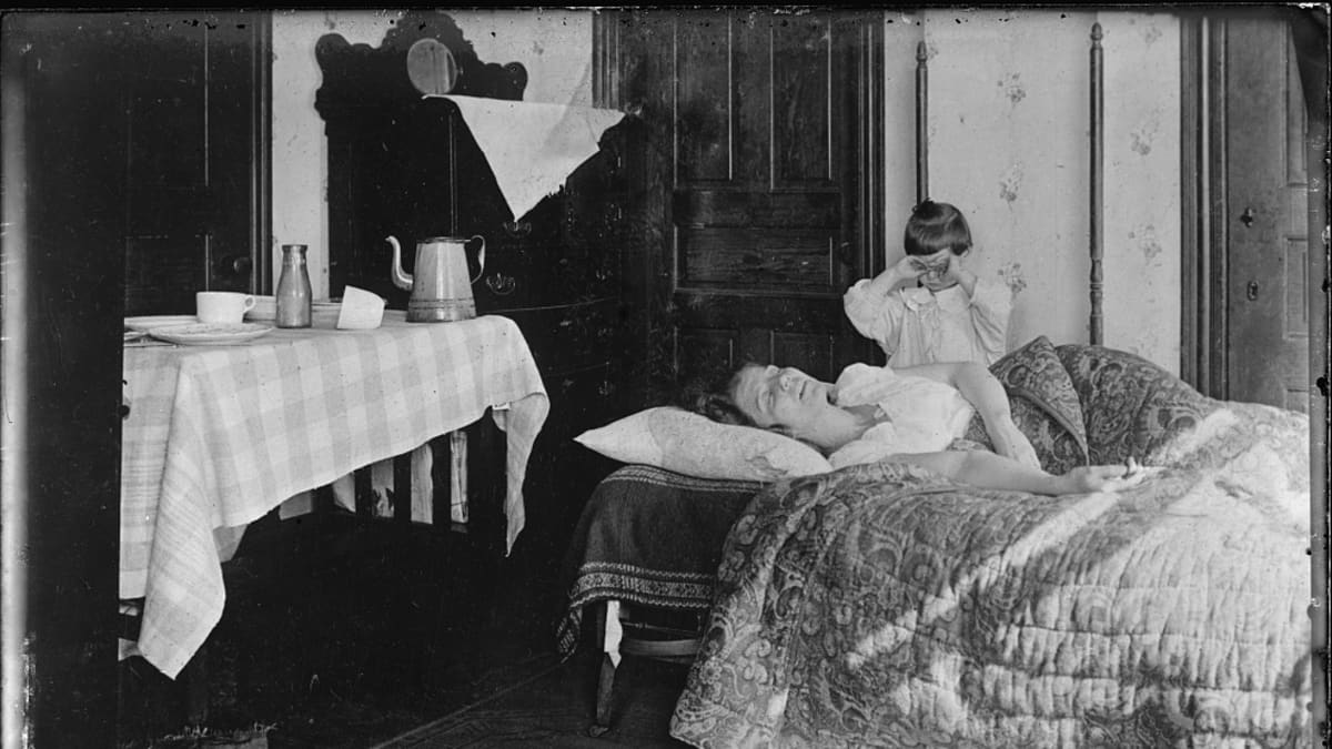 Mustavalkoinen valukuva sängyssä makaavasta naisesta ja vuoreen ääressä itkevästä pikkutytöstä. Influenssan merkki on vain lattialle pudonnut nenäliina.