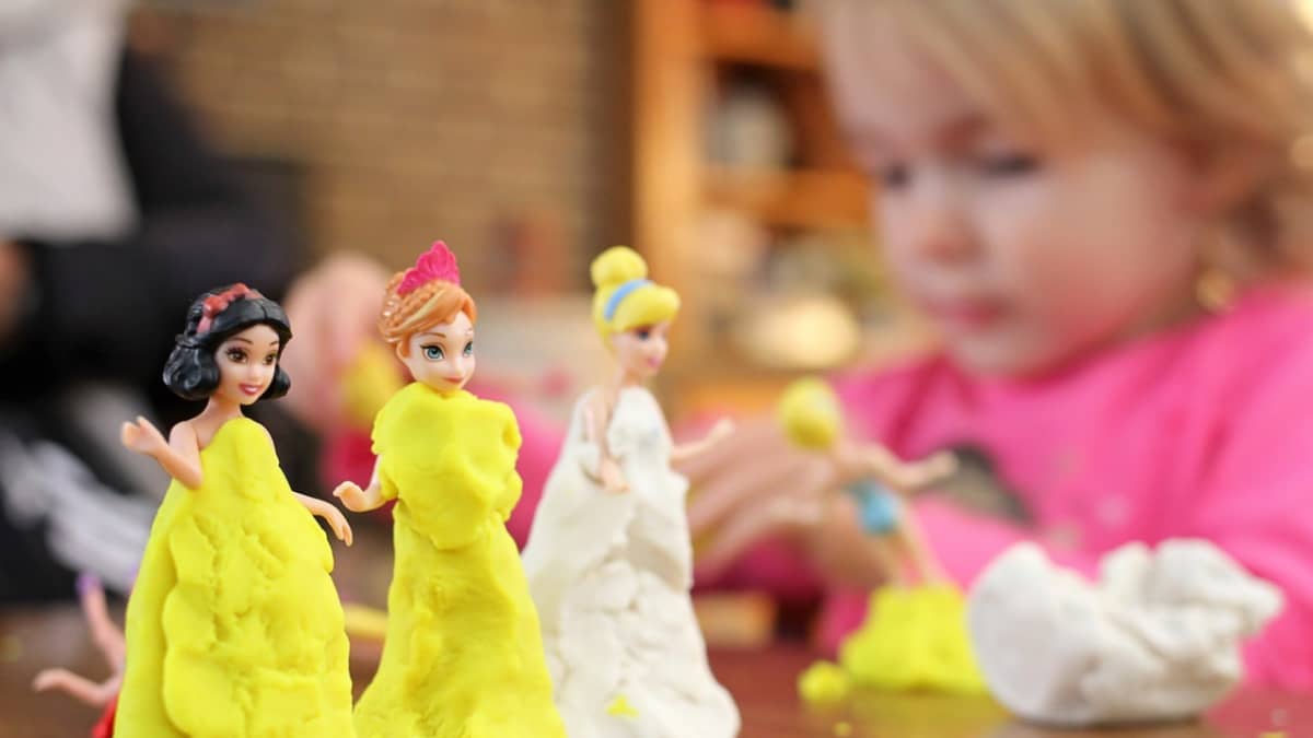 Pikkutyttö pukee pieniä Disney-nukkeja muovailuvahasta tehtyihin iltapukuihin.