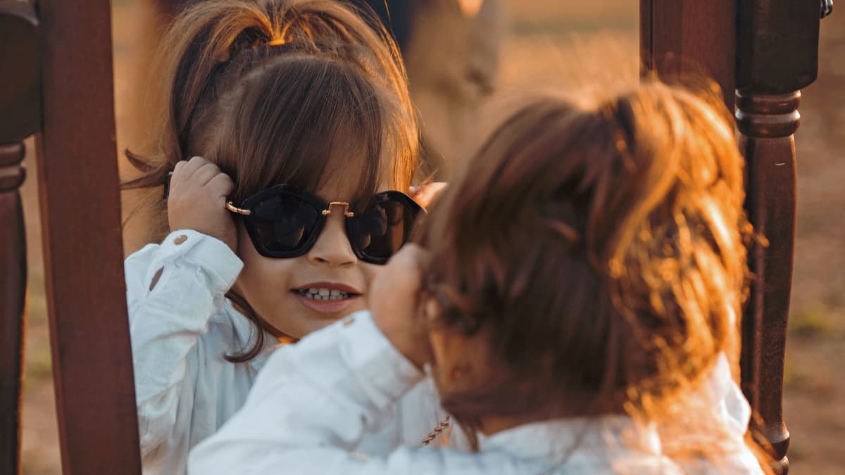 Pieni tyttö sovittelee aurinkolaseja peilin edessä.