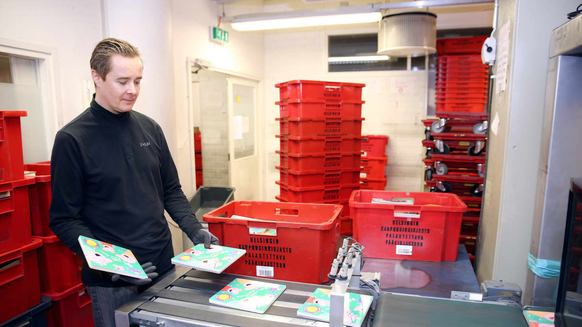 Virkailija käsittelee palautettuja kirjoja hihnalla Helsingin kaupunginkirjaston logistiikkayksikössä Pasilassa.