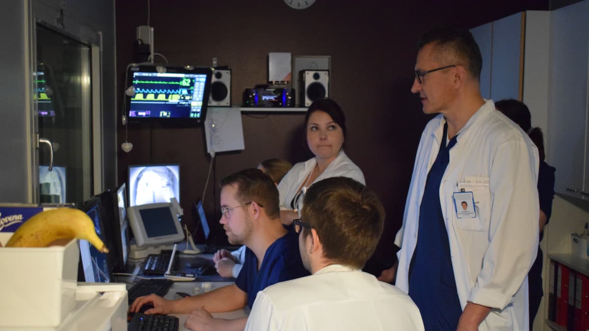 Tutkimusryhmä seuraa potilaan hoitoa valvomosta monitorien avulla.