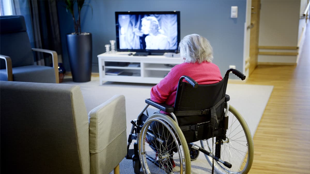 Vanhus pyörätuolissa katsoo televisiota.