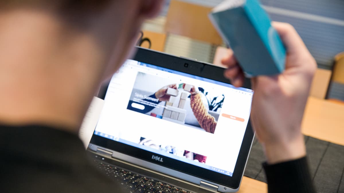 Mies selaa verkkopankkia avainlukulista kädessään.