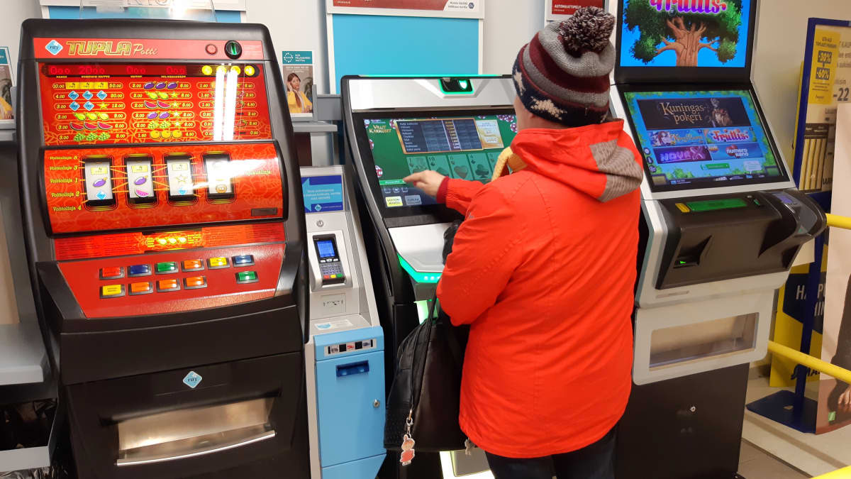 Punatakkinen nainen pelaa rahapeliautomaattia  kaupassa.