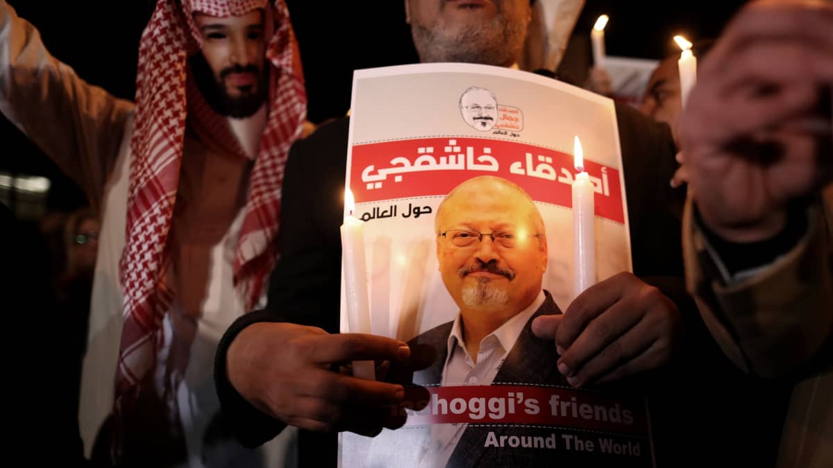 Mielenosoittaja piti Jamal Khashoggin kuvaa Istanbulissa lokakuussa 2018. Vasemmalla puolella toinen mielenosoittaja oli pukeutunut Saudi-Arabian kruununprinssiä esittävään naamariin. 
