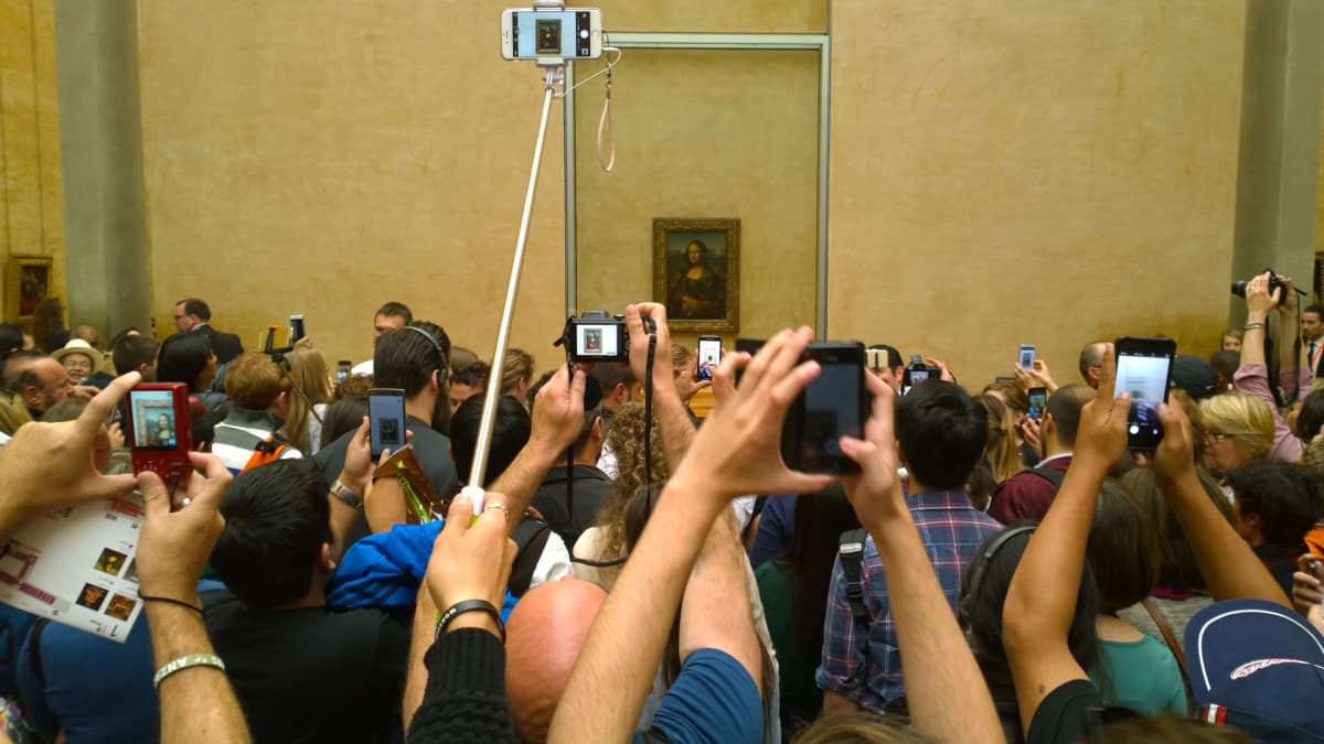 Takana maalaus Mona Lisasta ja sen edesää useita valokuvaajia ja turisteja
