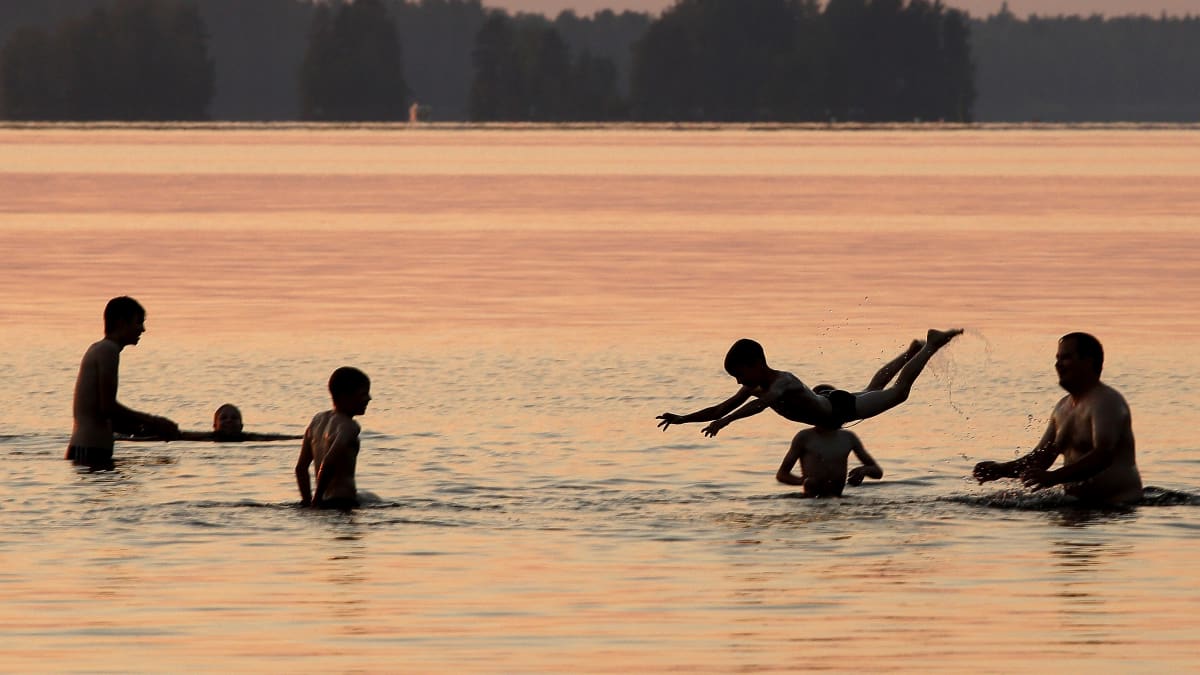 Aikuisia ja lapsia uimassa auringonlaskun aikaan.