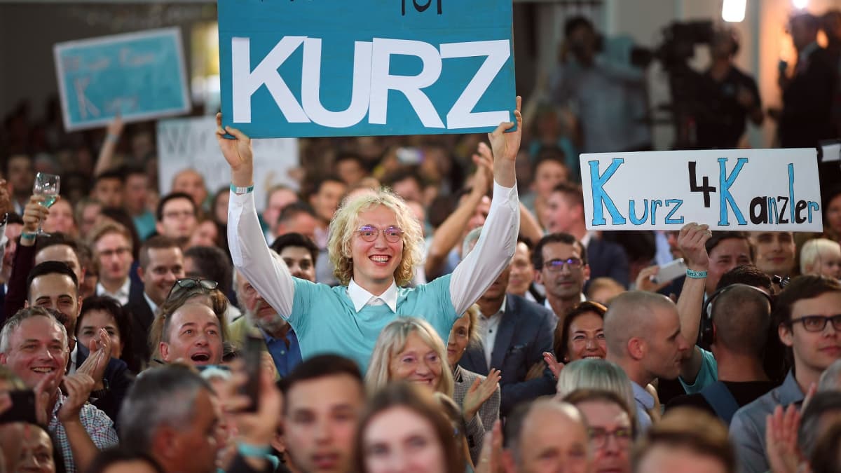 Ihmiset pitävät kylttejä, joissa osoitetaan tukea Sebastian Kurzille.