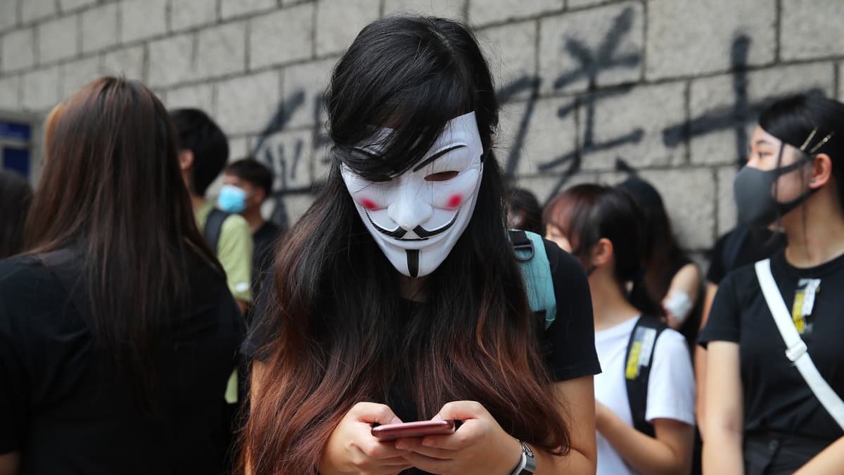 Nainen kirjottaa jotakin kännykällään Guy Fawkes maski kasvoilla