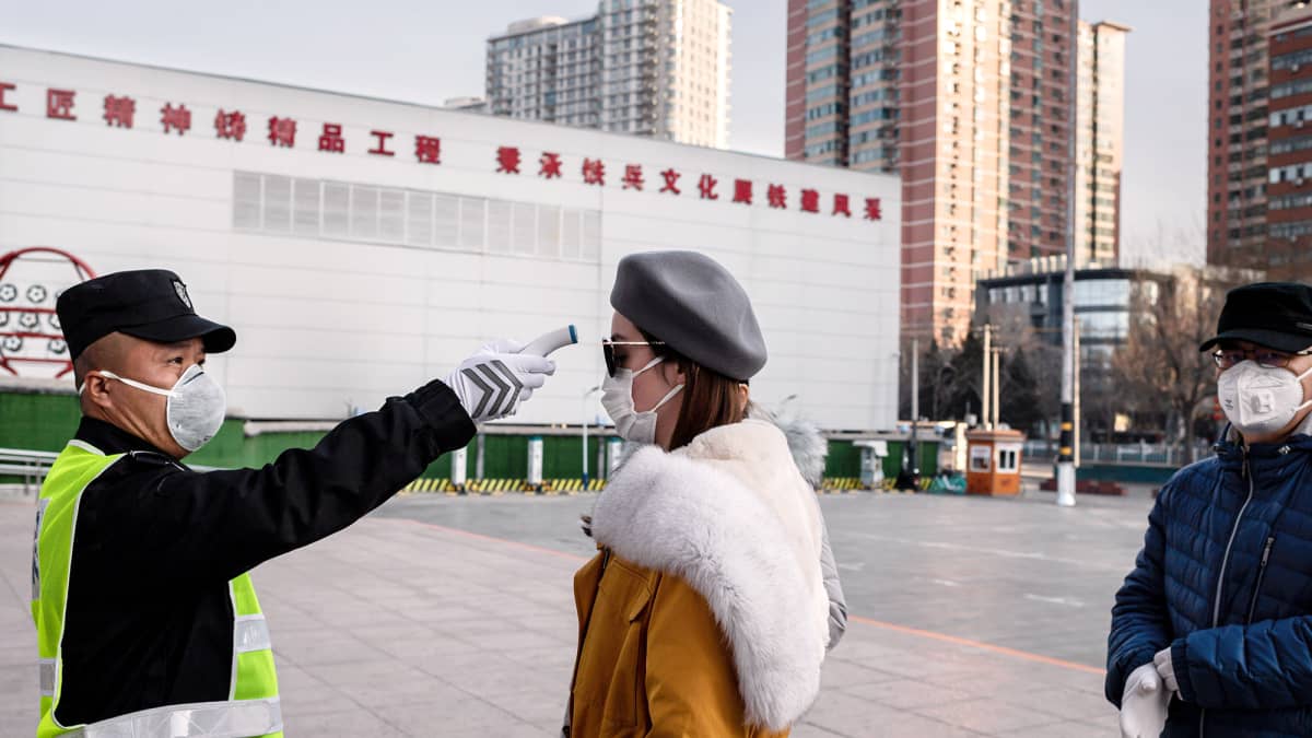 Vartija mittaa naisen kuumetta puiston sisäänkäynnillä Pekingissä.