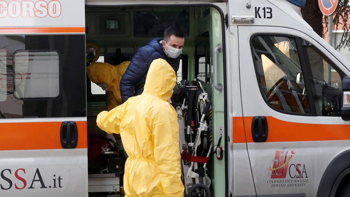 Suojapukuihin pukeutuneet terveystyöntekijät auttavat henkilöä ulos ambulanssista Italian Paduassa.