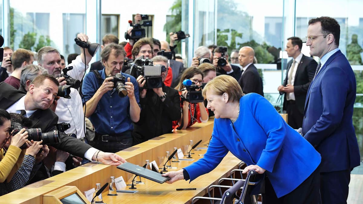 Saksan terveysministeri Jens Spahn ojentaa dokumentteja Angela Merkelille.