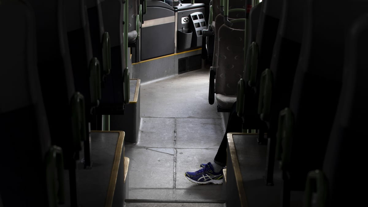 Matkustajan jalat tyhjällä bussin käytävällä.
