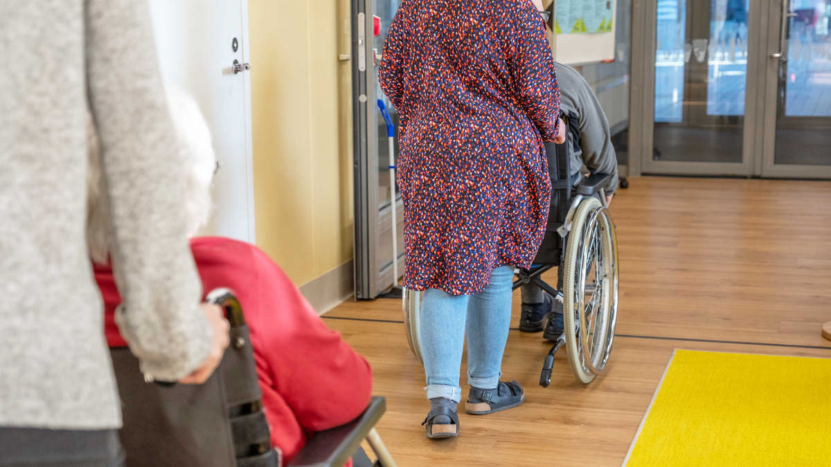 Työntekijät työntävät vanhuksia pyörätuolissa vanhustenkeskuksessa.