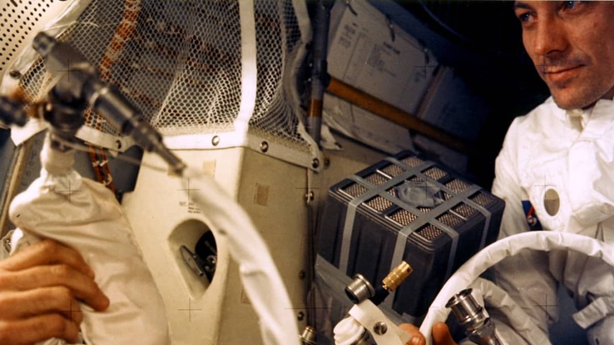 Laitteita ja kaksi astronauttia ahtaassa kuumoduulissa. Vasemmalla olevan astronautin kasvot eivät näy. 