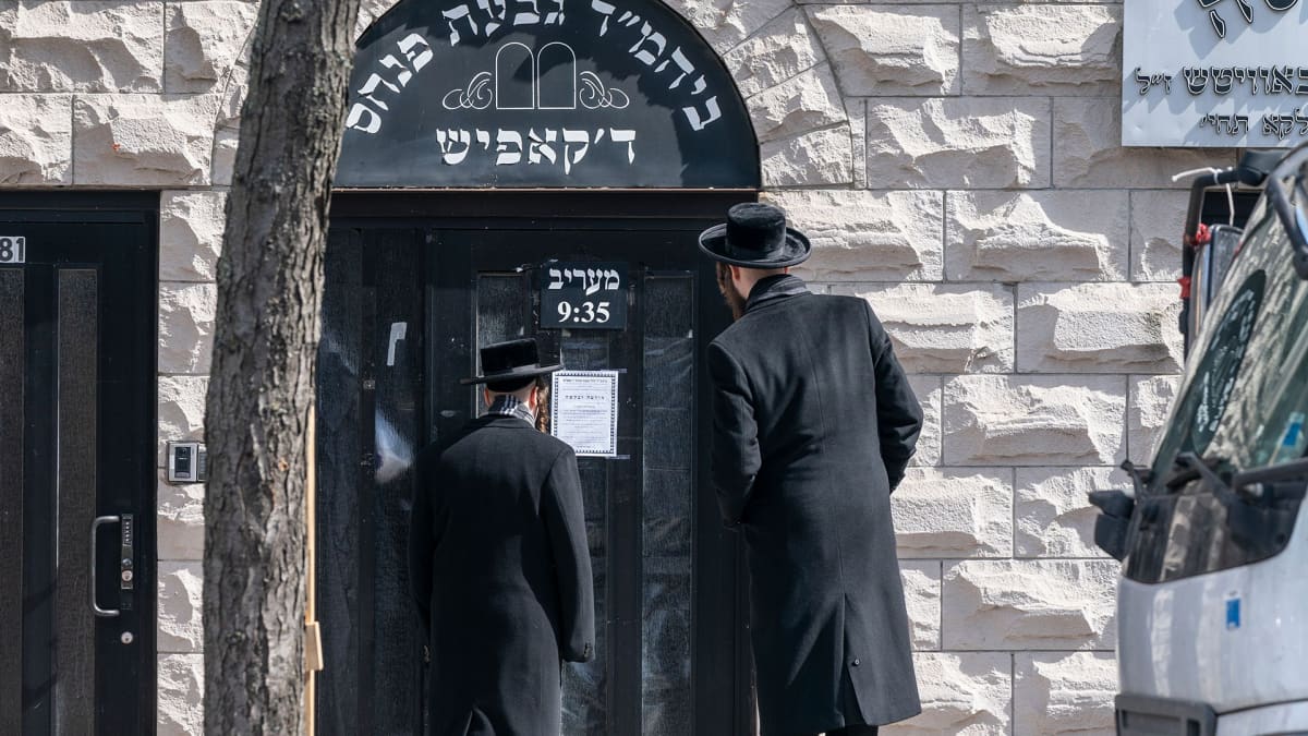 Hasidimiehet lukevat ilmoitusta koronavirksen sulkemasta synagogan ovesta.