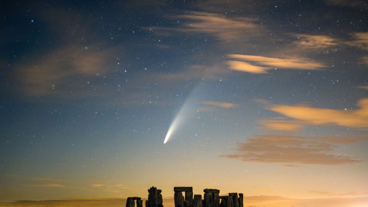 Stonehengen siluetti auringonlaskussa, taivaalla tähtiä ja komeetta. 