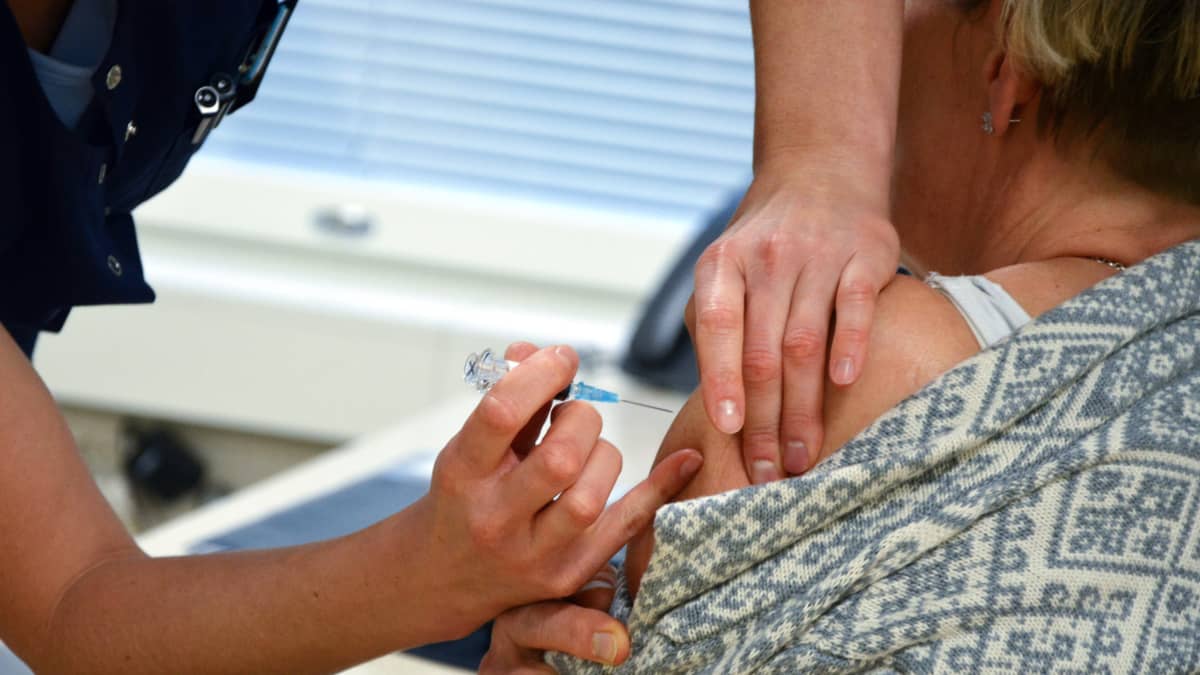 En hälsovårdare vaccinerar en kvinna genom att lägga en spruta i ena armen.